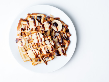 Belgian curd waffles with raspberries, banana, chocolate syrup.  Breakfast with tea on white background, top view, copy spaceの写真素材