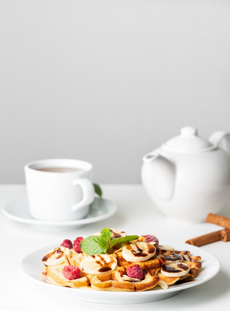 Belgian curd waffles with raspberries, banana, chocolate syrup.  Breakfast with tea on white backgroundの写真素材