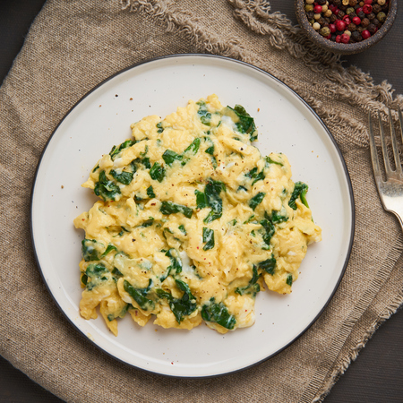 Pan-fried scrambled eggs and spinach, cup of tea on dark brown background. Breakfast with omelette, top viewの写真素材