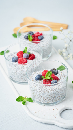 Chia pudding with fresh berries raspberries, blueberries. Three glass, vertical, light background, side view, flowersの写真素材