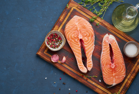 Two salmon steaks, fish fillet, large sliced portions  on chopping board on dark table. Top view, copy spaceの写真素材