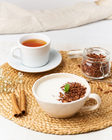 Yogurt with chocolate granola in cup, breakfast with tea on beige background, side view, verticalの写真素材