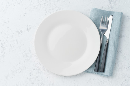 clean empty white plate, fork and knife on a white stone table, copy space, mock up, top view.