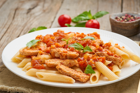 Penne pasta, chicken or turkey fillet, tomato sauce with a basil leaves on old rustic wooden background. Close up, side viewの写真素材