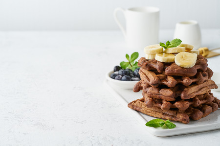 Chocolate banana waffles with maple syrup on a white table, copy space, side view.の写真素材