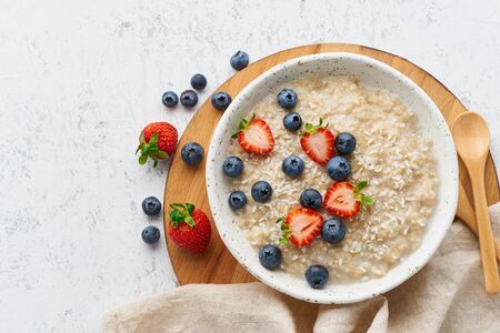 Oatmeal rustic porridge with blueberry, bilberry, blackberry, strawberry, dash diet, wooden white background, top viewの写真素材