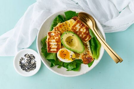 keto ketogenic diet soft boiled eggs with grilled haloumi, avocado and lettuce, mediterranean cuisine on pastel backgroundの写真素材