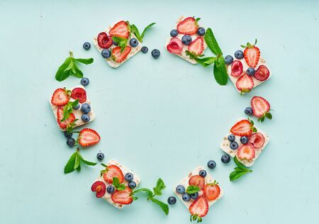 vegeterian dieting rise crispbread frame with berries: strawberry, blueberry, bilberry, blackberry and banana on pastel turquoise aquamarine background top viewの写真素材
