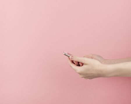 woman hand without manicure hold phone on pastel pink background with copy space