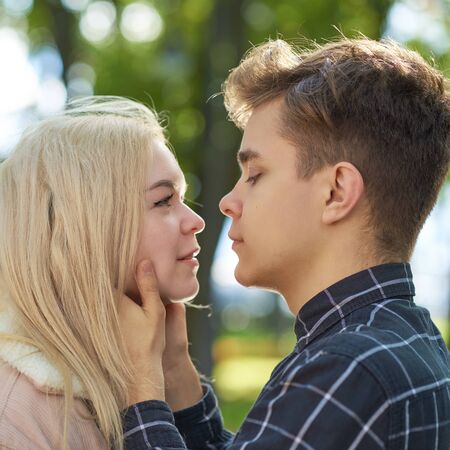 The boy looks tenderly at the girl, hands clasped her face and wants to kiss. Concept of teenage...