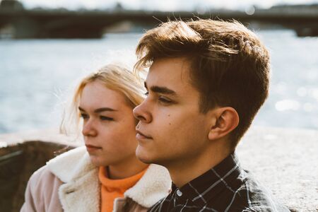 Teenagers in love sit on the waterfront in the city center, resting in the autumn sun. Concept the...
