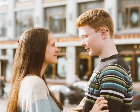 Male and female person looking at each other, young couple full of love. The redhead boy looks tenderly at girl and kiss. Concept of a teenage love and first kiss, love, relationship. City, waterfront.の写真素材