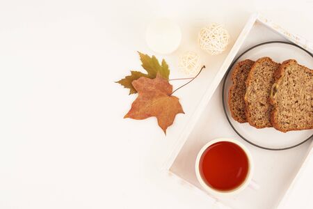 Autumn food-slices of banana bread, a Cup of tea, dry leaves, a white wooden table. Cozy home...