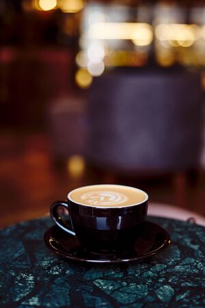 A Cup of cappuccino with foam on a marble table in a cozy little cafe. Drink with vegetable milk,...
