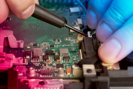 Man repairs computer. A service engineer in a shirt repairs a laptop, at a white Desk against a...