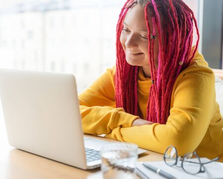 A woman is looking at a laptop and smiling. Live chat, stream. Girl with long pink hair, designer,...