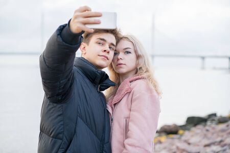 Loving teenagers on date. Cute brunette boy and beautiful blonde girl take a selfie on a cell phone....