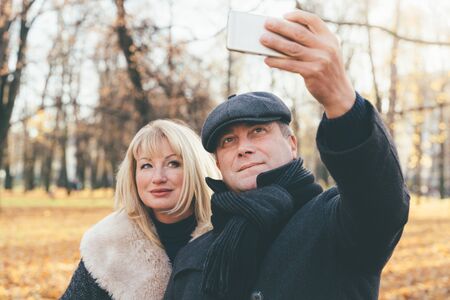 Happy blonde mature woman and beautiful middle-aged brunette take selfie on mobile phone.