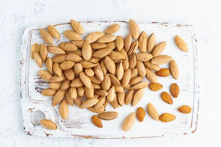 Top view almonds in endocarp, bowl with drupe in shell on a white wooden cutting board. White background, overhead, copy space, close upの写真素材