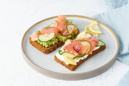 Smorrebrod - traditional Danish sandwiches. Black rye bread with salmon, cream cheese, cucumber, avocado on a wooden backgroundの写真素材