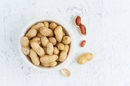 Top view plate with peanut in a endocarp, bowl with drupe in shell on a white table. Stone...