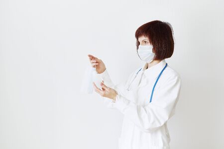 Female doctor in medical mask and uniform offers mask and disinfectant in bottle to prevent from coronavirus. Covid-19 protection, medical information. Copy spaceの写真素材