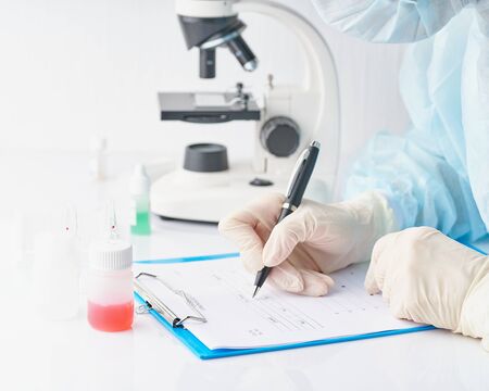 Pandemic COVID-19, Coronavirus. Doctor in hospital is on duty, avail for work, filling out forms. Woman in uniform and face mask conducts tests in laboratory, writes down results. Selective focusの写真素材