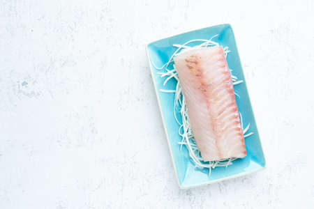 Fillet of raw white walleye fish on a blue plate on a white background. Top view, copy space.