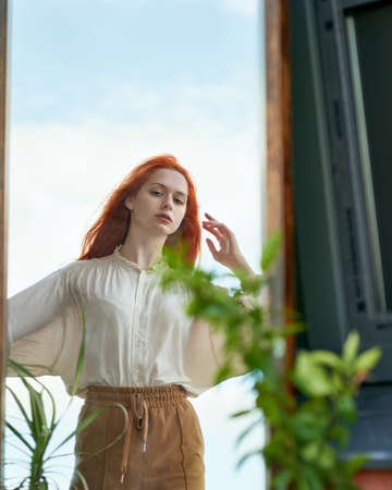 Beautiful red-haired woman looks at reflection in mirror on streetの写真素材