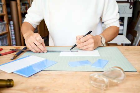 Faceless female entrepreneur cutting glass in artisan workroom. Business woman draws line on plate,...