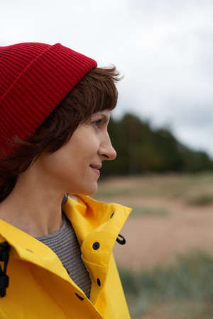 One with nature. Crop closeup portrait of mature beautiful woman in bright yellow jacket and red hat...