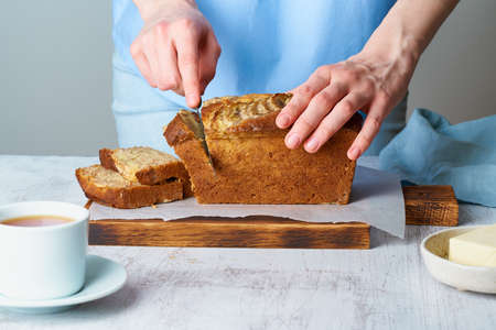 Woman cuts banana bread on a wooden board. Cake with banana
