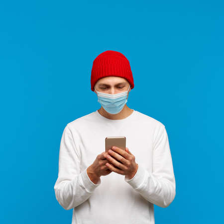 Portrait of man with medical protective face mask, texting on mobile phone. Male write message...