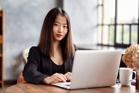 Asian business woman working in laptop in office. Japanese businesswoman work in cafe. Active serious smart female worker looking at cameraの写真素材