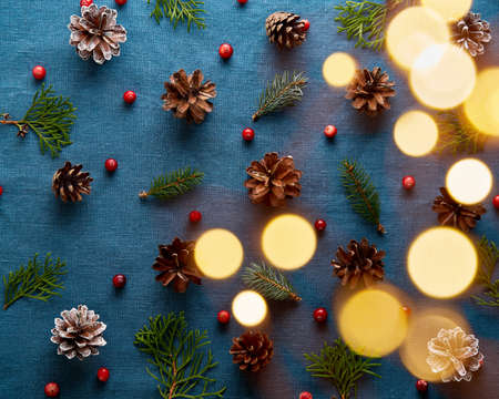 Christmas and Happy New Year dark blue background. Pattern with golden light glow garland bokeh and fir branches, cones, cranberry berries. Textile backdrop with copy space.の写真素材