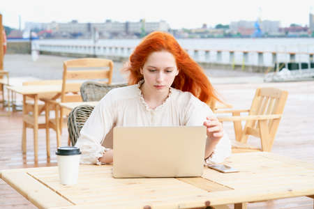 Redhead female looking at laptop in cafe outsideの写真素材