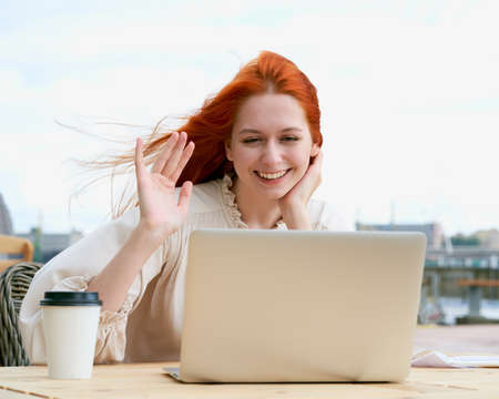 Cheerful redhead female chatting on laptop in cafe outsideの写真素材