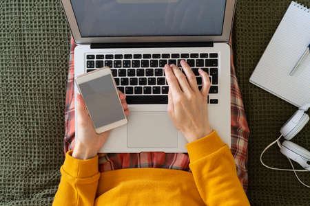 Online shopping. Woman typing code and password from message on phone on laptop.