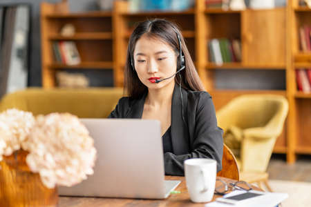 Asian businesswoman in headset speaking by conference call and video chat