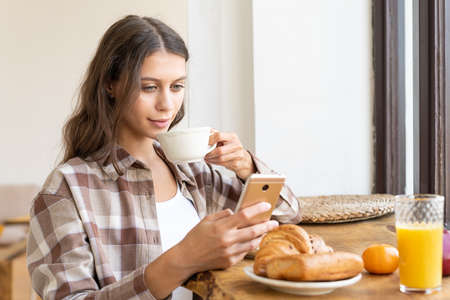 Woman viewing social networks using mobile, enjoying healthy breakfast. Concept for digital addiction, morning routine. Sunday slow lifeの写真素材