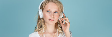Long width banner with portrait of young woman listening music via headphones on color neutral tone...