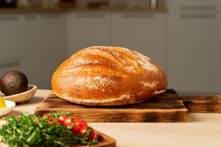 Whole loaf of freshly baked white wheat bread on wooden board on home kitchen table, copy space,...