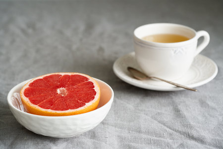 Still life with half of grapefruit in bowl and cup of herb tea on table covered with crumpled gray tablecloth in natural light from window. Lifestyle photoの写真素材