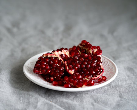 Still life with broken open pomegranate and seeds on plate on table covered with crumpled gray tablecloth in natural light from window. Lifestyle photo with bright red center on neutral backdropの写真素材
