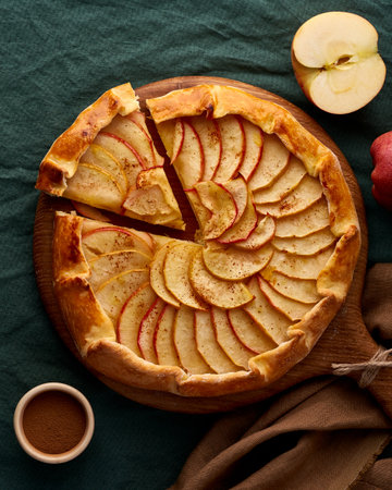 Apple pie, galette with fruits, sweet pastries on dark green tablecloth, sweet crostata on cutting wooden board, side view, autumn or winter food, vertical, top viewの写真素材