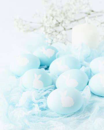 Easter. Holiday. Light white background, gentle pastel colors. Blue eggs with image of rabbit in...