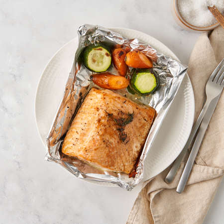 Foil pack dinner with fish. Fillet of salmon with vegetables on white plate - zucchini, carrots. Healthy diet food, keto diet, Mediterranean cuisine. Top viewの写真素材