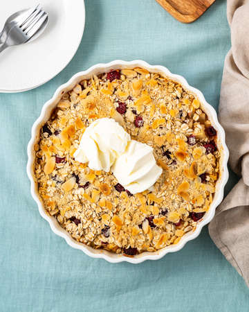 Apple and pear crumble with ice cream, streusel. Sweet dessert with oats stewed fruit topped crisp crumbly mixture served ice cream. Apple cobbler pie in baking dish on tablecloth. Top view, vertical