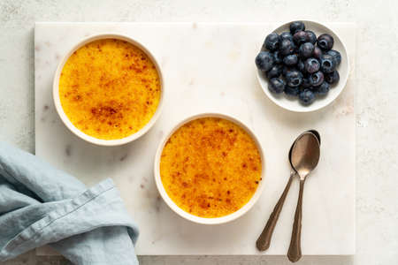 Two ramekin with Creme brulee. Traditional French vanilla cream dessert. Spanish crema catalana, rich custard base. Top view, copy space, marble backgroundの写真素材