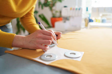 Cropped shot of woman seamstress making sewing pattern on yellow piece of tissue at her creative...